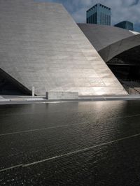 a photo of a big structure with water in it with people walking around it, and people walking about in front