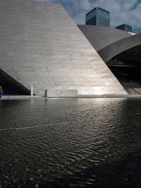 a photo of a big structure with water in it with people walking around it, and people walking about in front