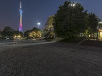 a brick paved square at night with a tall tower in the background on one side of the road