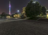 a brick paved square at night with a tall tower in the background on one side of the road