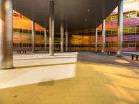 an empty courtyard that has colorful windows on it and benches lined in the background are on concrete