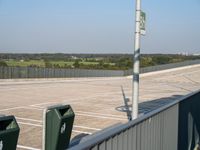 an empty parking lot with green trash cans on the ground and trees in the background