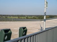 an empty parking lot with green trash cans on the ground and trees in the background