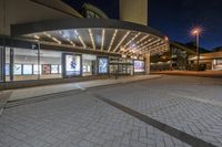 a picture of a building on the road at night with lights illuminating through glass and windows