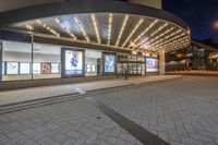 a picture of a building on the road at night with lights illuminating through glass and windows