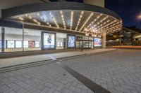 a picture of a building on the road at night with lights illuminating through glass and windows