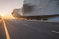 street with the sun setting and a building in the background that is the curve of a large structure