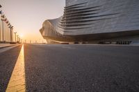 street with the sun setting and a building in the background that is the curve of a large structure