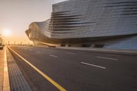 street with the sun setting and a building in the background that is the curve of a large structure