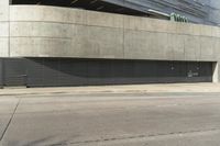 a view from the street of an empty parking lot that is under a building with concrete exterior and doors