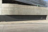 a view from the street of an empty parking lot that is under a building with concrete exterior and doors