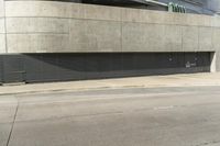 a view from the street of an empty parking lot that is under a building with concrete exterior and doors