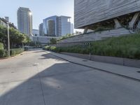 a paved, empty city street with grass along the sides and modern architecture on the hill