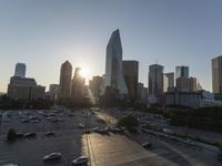 the sun is setting over a city with tall buildings and cars in a parking lot