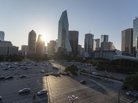 the sun is setting over a city with tall buildings and cars in a parking lot