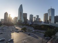 the sun is setting over a city with tall buildings and cars in a parking lot