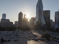 the sun is setting over a city with tall buildings and cars in a parking lot