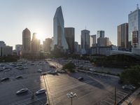 the sun is setting over a city with tall buildings and cars in a parking lot