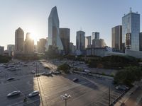 the sun is setting over a city with tall buildings and cars in a parking lot