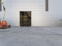 a man in a boom is next to an orange crane with a door opening into a large storage building