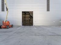 a man in a boom is next to an orange crane with a door opening into a large storage building