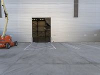 a man in a boom is next to an orange crane with a door opening into a large storage building