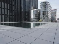 an empty pool in front of a very large building with black windows and glass walls