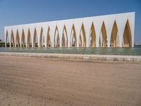 a large building with golden colored columns in front of the water on a beach area