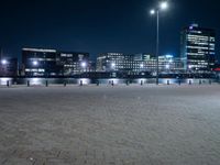 the lights are on at night beside the buildings and water below them, along with an empty brick sidewalk