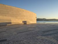 a curved concrete building with benches on the top and two smaller stone buildings below it