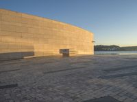 a curved concrete building with benches on the top and two smaller stone buildings below it