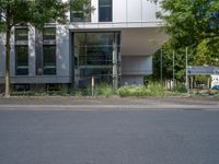 a large building with an entrance on a city street lined by tall green trees, and a small bench near it