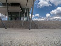 a person on a bike walking through a stone building entrance, in front of an enormous glass wall and stairs