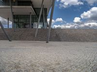 a person on a bike walking through a stone building entrance, in front of an enormous glass wall and stairs