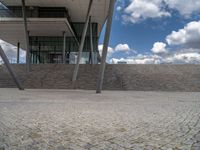 a person on a bike walking through a stone building entrance, in front of an enormous glass wall and stairs