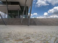 a person on a bike walking through a stone building entrance, in front of an enormous glass wall and stairs