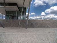 a person on a bike walking through a stone building entrance, in front of an enormous glass wall and stairs