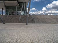 a person on a bike walking through a stone building entrance, in front of an enormous glass wall and stairs