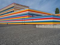 an empty parking lot painted brightly stripes on the wall of the building and sky as well as stones