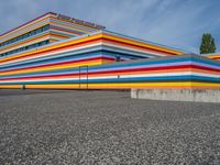 an empty parking lot painted brightly stripes on the wall of the building and sky as well as stones