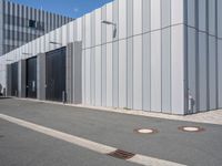 an industrial building with four metal doors and two drainage covers on either side of the walkway