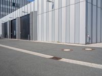 an industrial building with four metal doors and two drainage covers on either side of the walkway