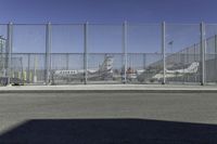 a gate with airplanes parked behind it next to a road and parking lot in the sun