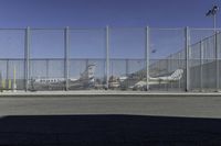 a gate with airplanes parked behind it next to a road and parking lot in the sun