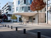 a person standing by a building on the street in front of it and one man walking past them