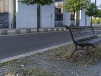 a park bench by the side of a road near a building with a large window