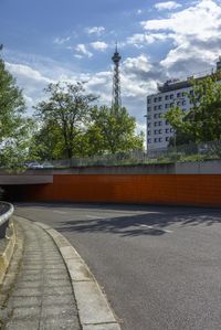 an asphalt street with a bridge and an orange wall in the background with a cloudy blue sky