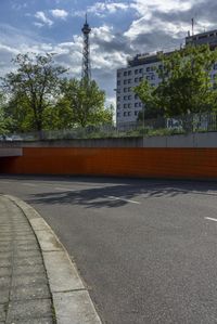 an asphalt street with a bridge and an orange wall in the background with a cloudy blue sky