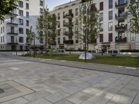 a paved walkway surrounded by grass and tall buildings next to a path with a tree in the middle