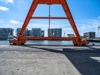 a man is sitting under the big orange structure at a boat dock on a lake